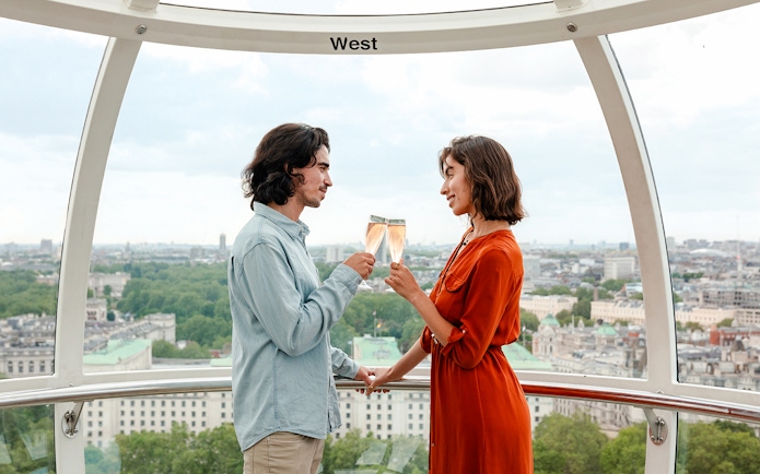 Couple toasting with champagne inside the London Eye capsule, overlooking cityscape.