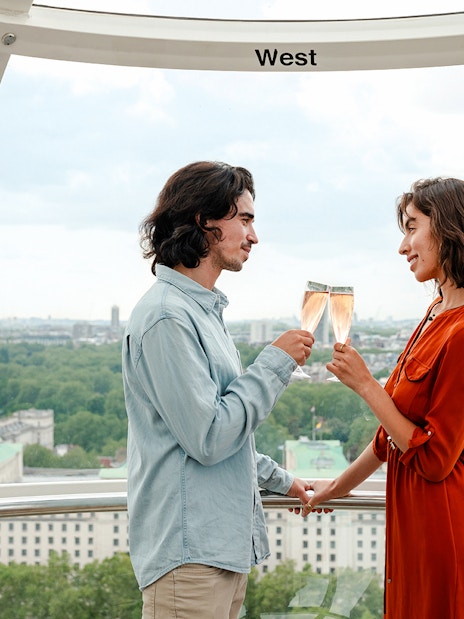 Couple toasting with champagne inside the London Eye capsule, overlooking cityscape.