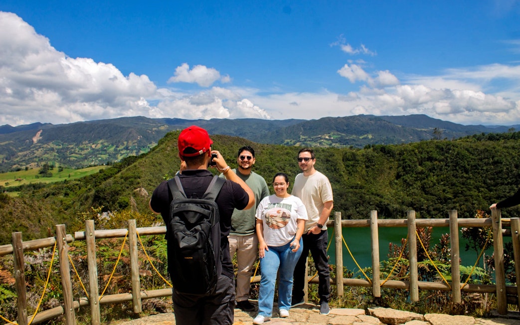 Visitors posing in front of Guatavita Lake, Colombia, with scenic mountain backdrop.