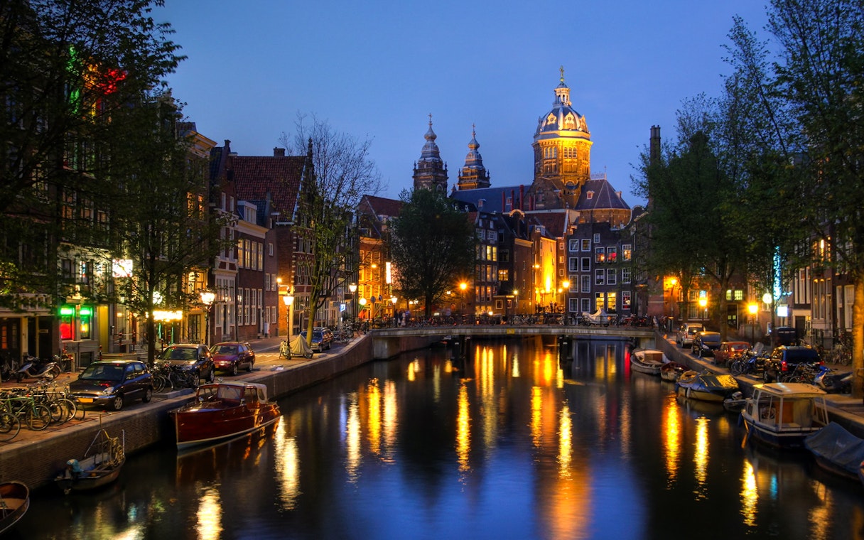 Amsterdam canal view with illuminated buildings and boats at dusk.