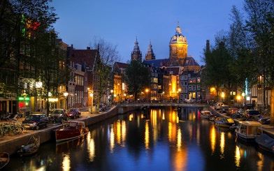 Amsterdam canal view with illuminated buildings and boats at dusk.