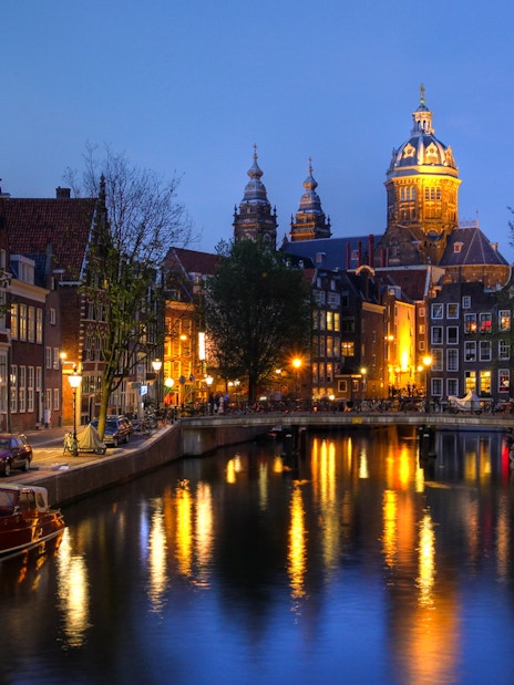 Amsterdam canal view with illuminated buildings and boats at dusk.
