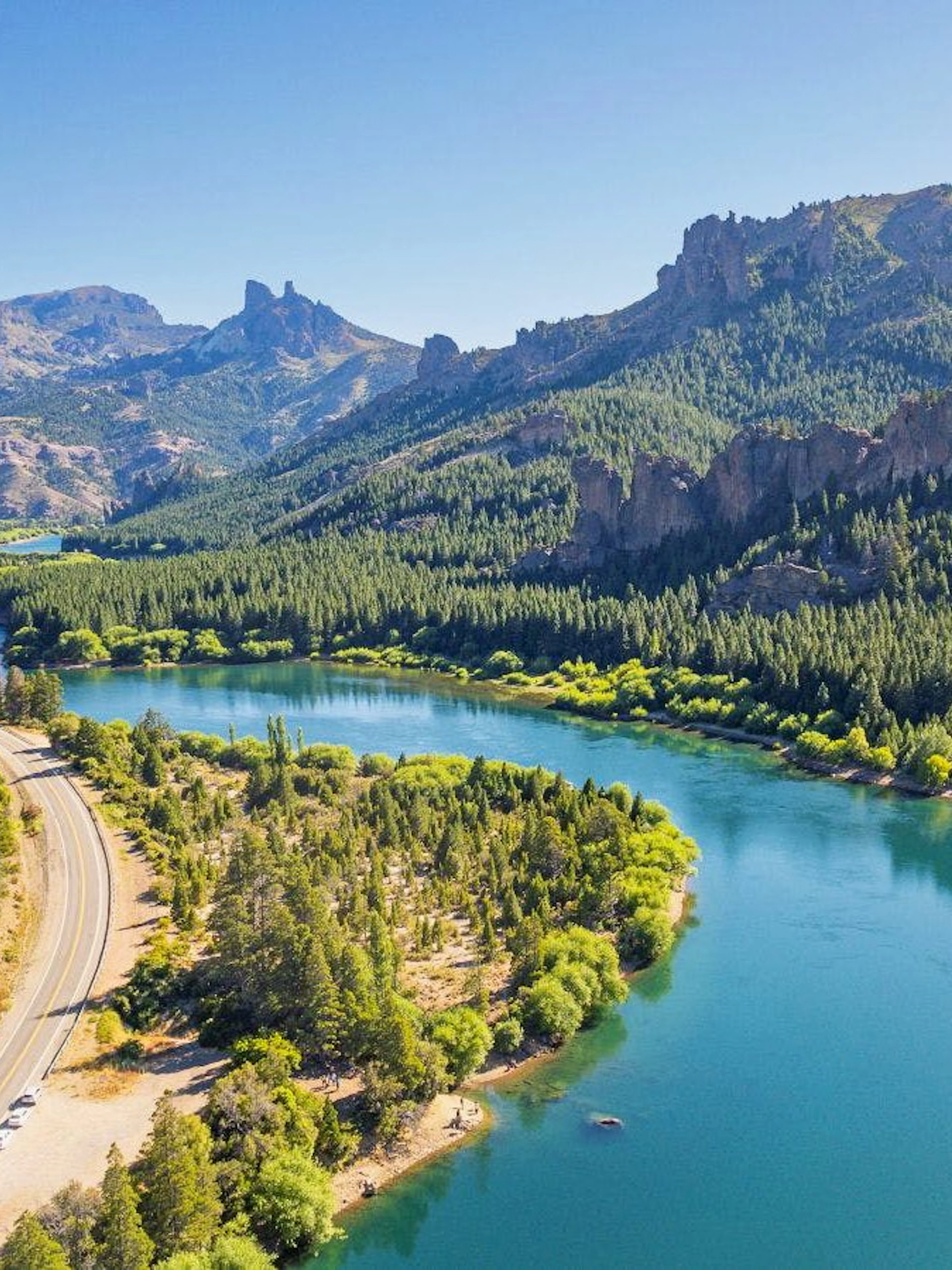 Winding road beside turquoise lake in Patagonia near Bariloche, surrounded by forested mountains.