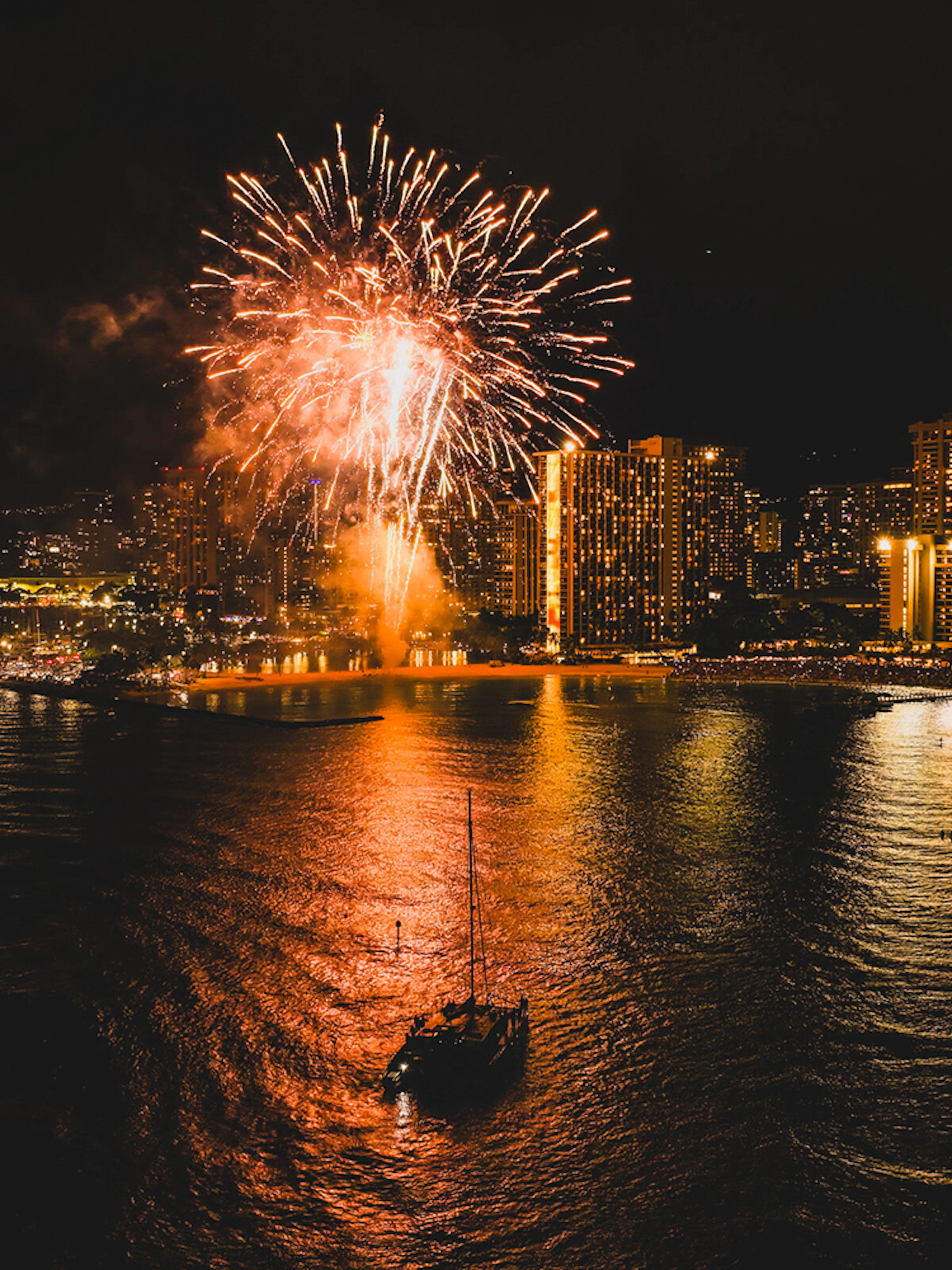 Sailboat on Waikiki waters with fireworks illuminating the night sky.