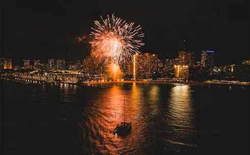 Sailboat on Waikiki waters with fireworks illuminating the night sky.