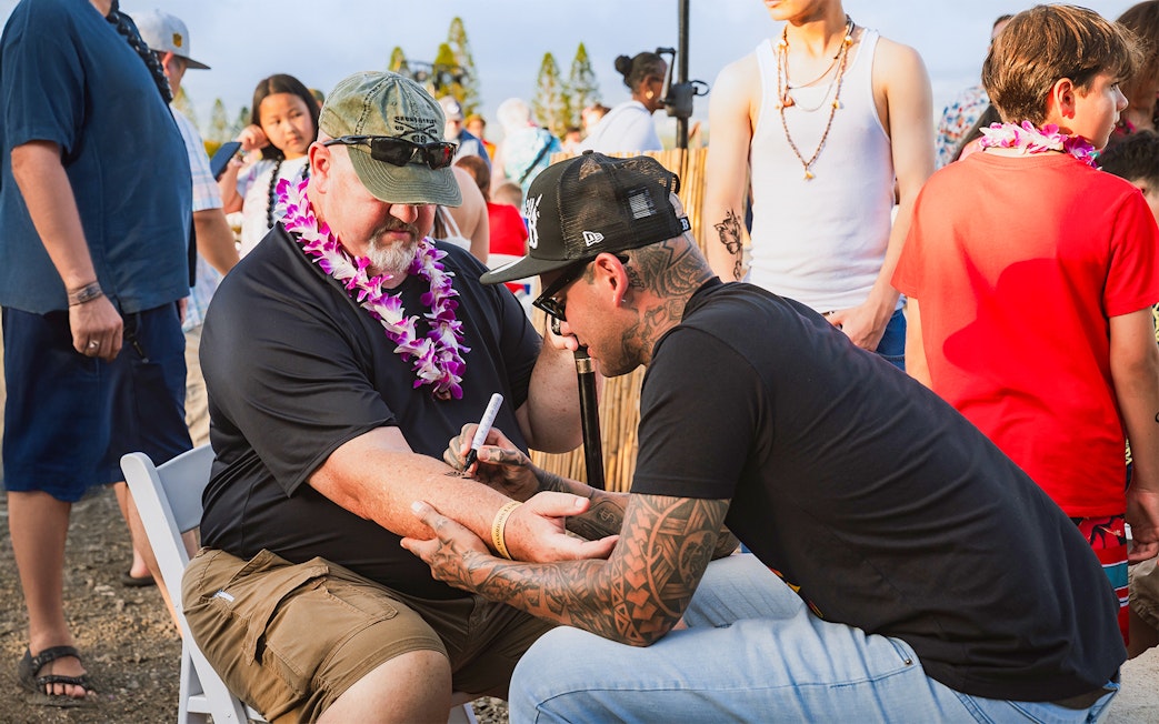 Man receiving traditional Hawaiian tattoo on arm at Mauka Warriors Luau.