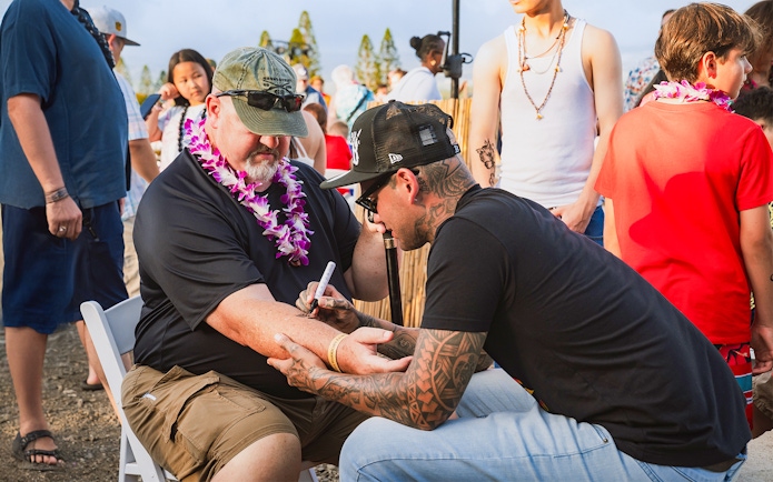 Man receiving traditional Hawaiian tattoo on arm at Mauka Warriors Luau.