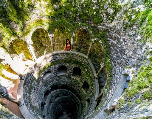Quinta Da Regaleira initiation well in Sintra, Portugal, showcasing spiral staircase and lush greenery.