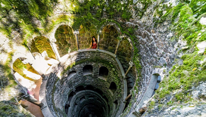 Quinta Da Regaleira initiation well in Sintra, Portugal, showcasing spiral staircase and lush greenery.