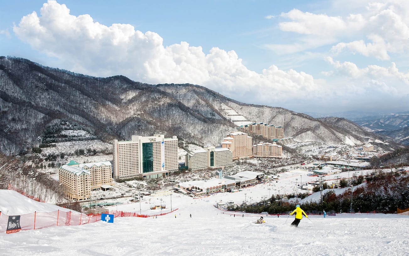Skiers on snowy slopes at Vivaldi Park Ski World with mountain backdrop, near Seoul.