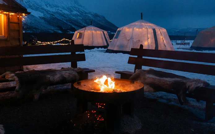 Bonfire surrounded by benches and tents in snowy Tromso Lapland.