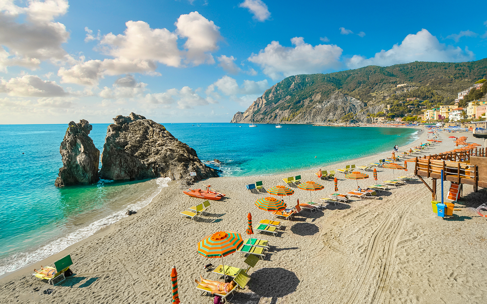 Beach with colorful umbrellas and sunbathers in Cinque Terre, Italy, part of a guided tour from Florence.