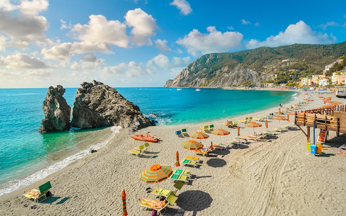 Beach with colorful umbrellas and sunbathers in Cinque Terre, Italy, part of a guided tour from Florence.