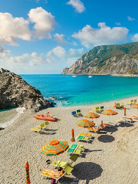 Beach with colorful umbrellas and sunbathers in Cinque Terre, Italy, part of a guided tour from Florence.