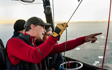 Guests pointing at landscape from hot air balloon basket.