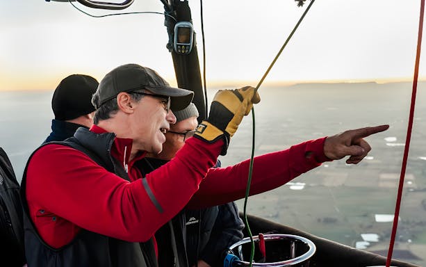 Guests pointing at landscape from hot air balloon basket.