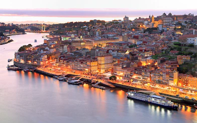 Porto skyline and Douro River at sunset with illuminated buildings.