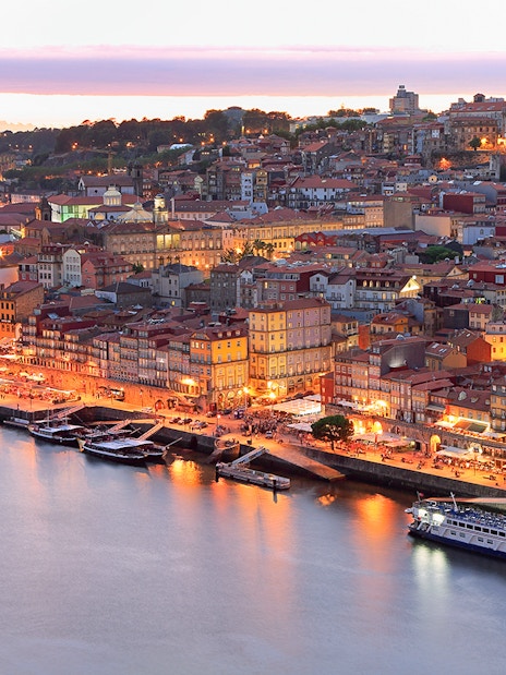 Porto skyline and Douro River at sunset with illuminated buildings.