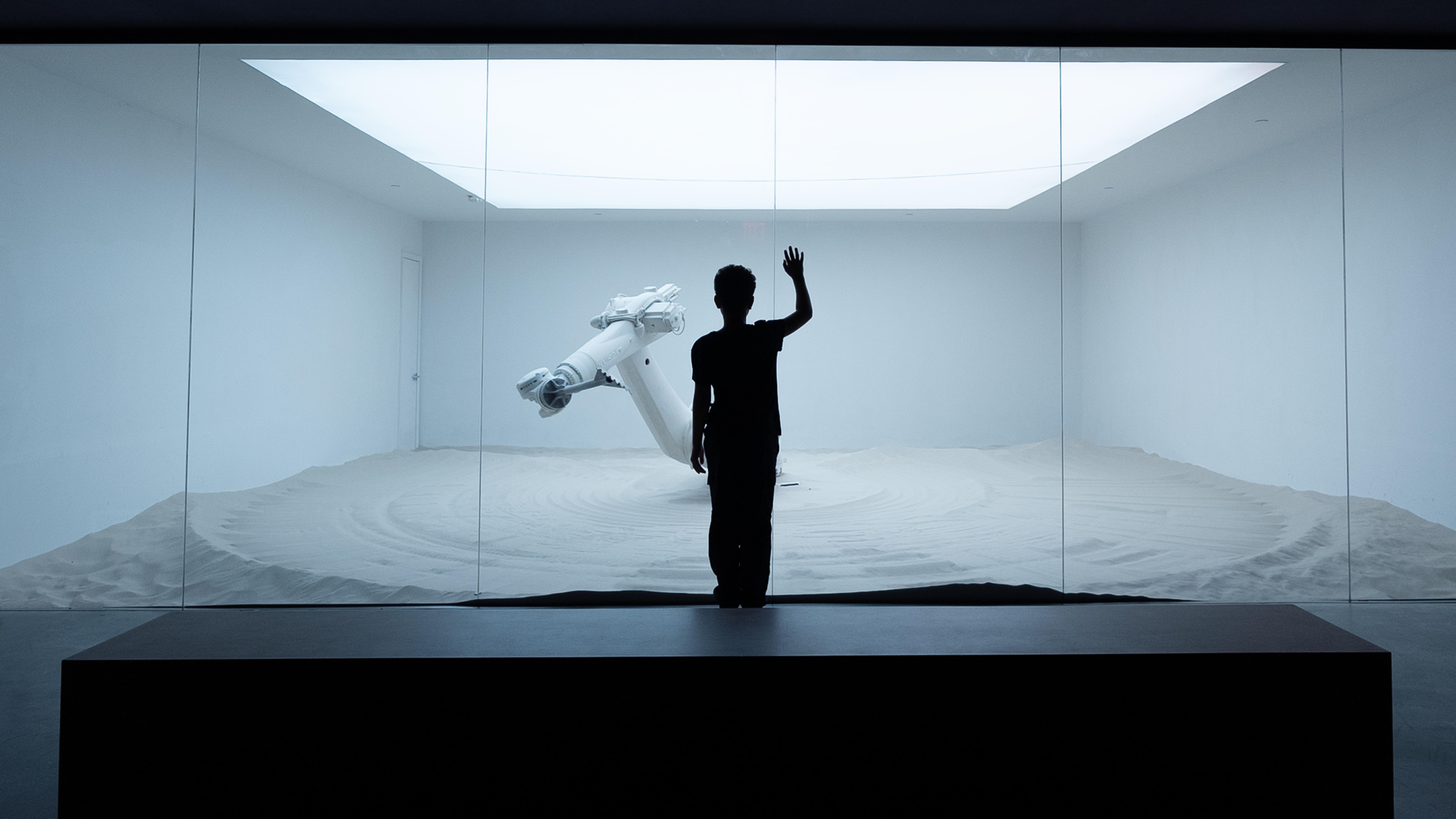Silhouette of a person observing a robotic arm in a sand-filled exhibit at Mercer Labs: Museum Of Art & Technology.