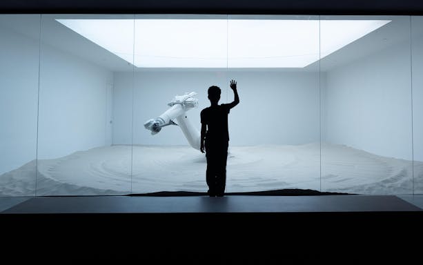 Silhouette of a person observing a robotic arm in a sand-filled exhibit at Mercer Labs: Museum Of Art & Technology.