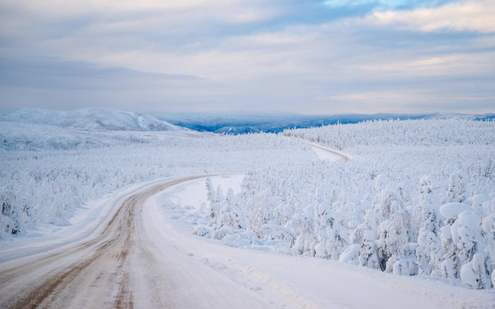 Dalton Highway in Alaska covered in snow, winding through a snowy forest landscape.