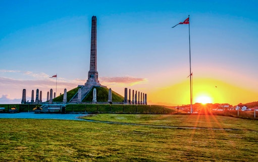 Norwegian national monument at sunset with flag and obelisk.