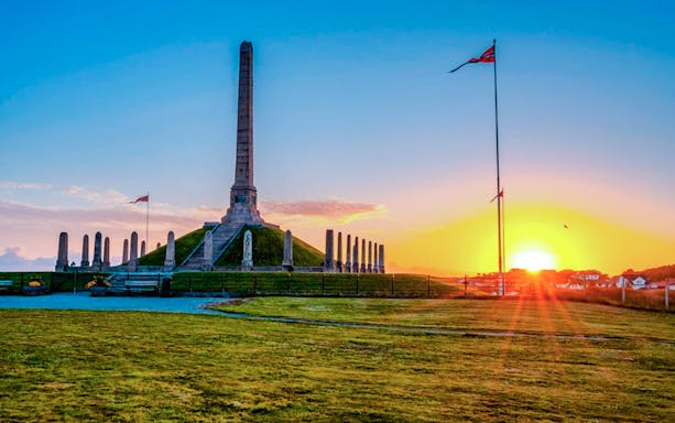 Norwegian national monument at sunset with flag and obelisk.