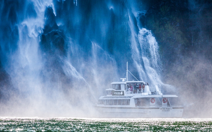 Cruise boat near waterfall at Milford Sound, New Zealand.