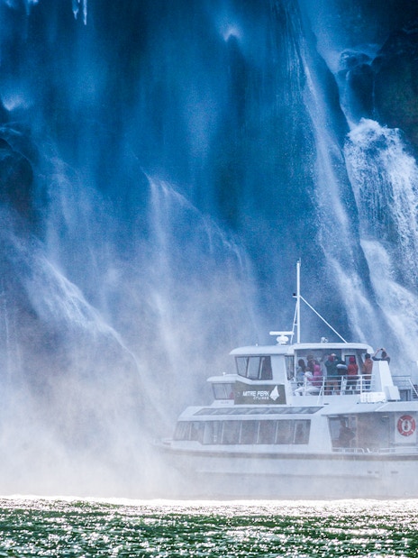 Cruise boat near waterfall at Milford Sound, New Zealand.