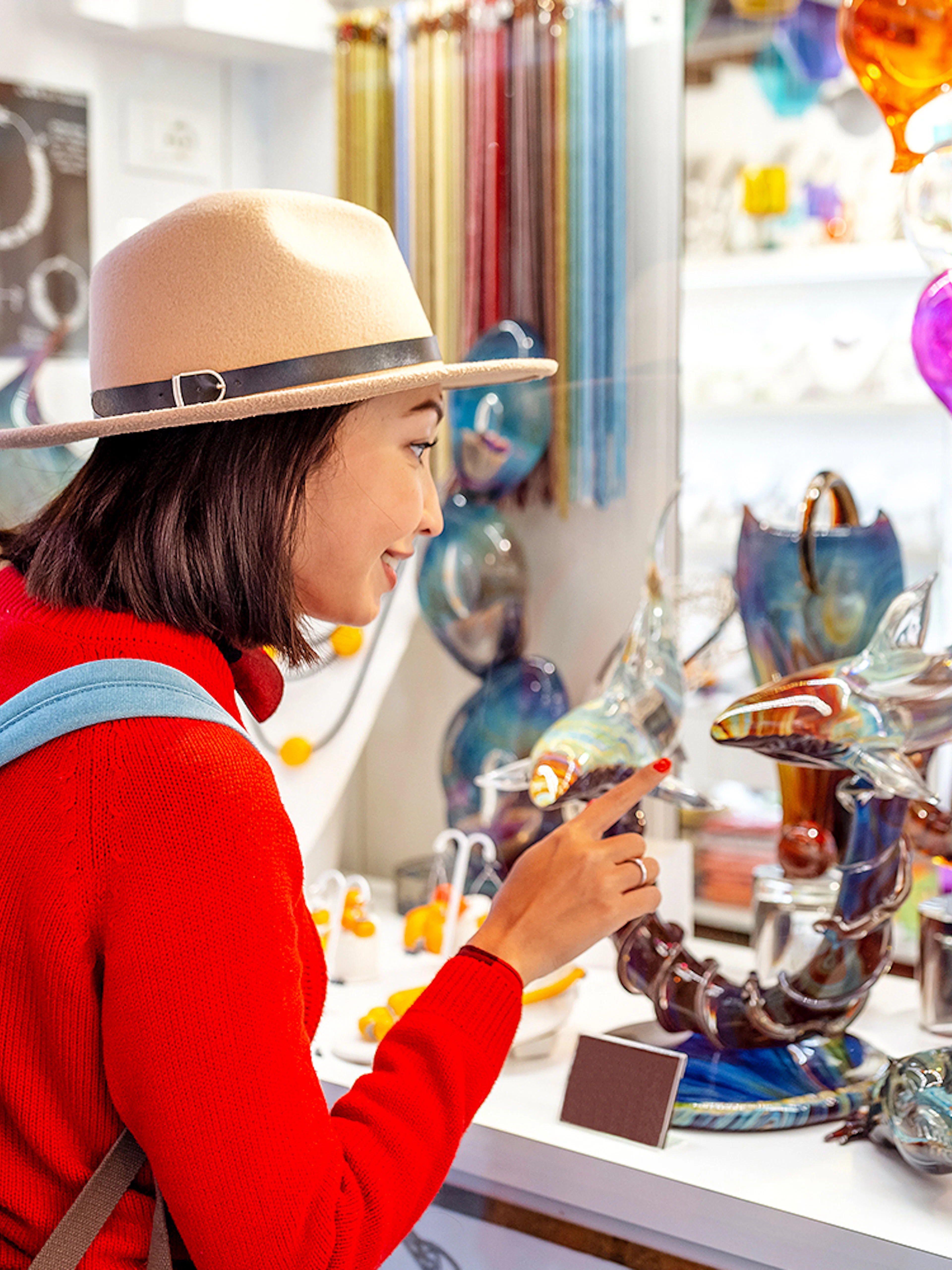 Tourist exploring glass art at Murano glass factory, colorful glass balloons and sculptures displayed.