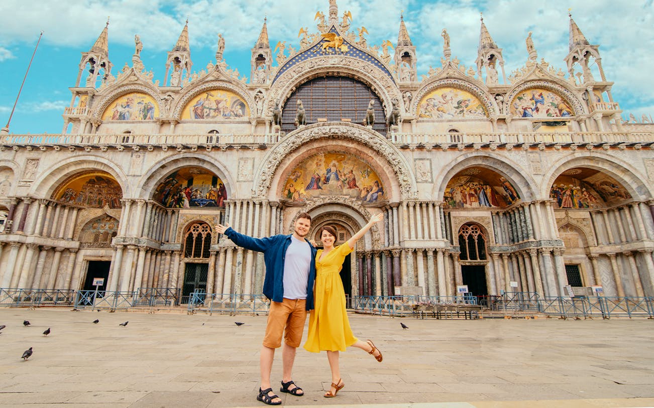 Visitors in front of St. Mark's Basilica, Venice, with intricate facade details.