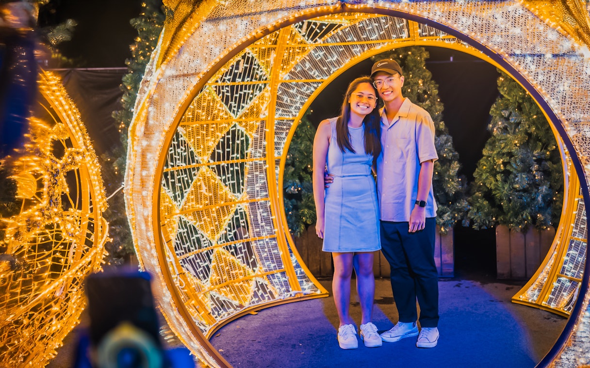 Couple standing under illuminated arches at Gardens by the Bay during Christmas.