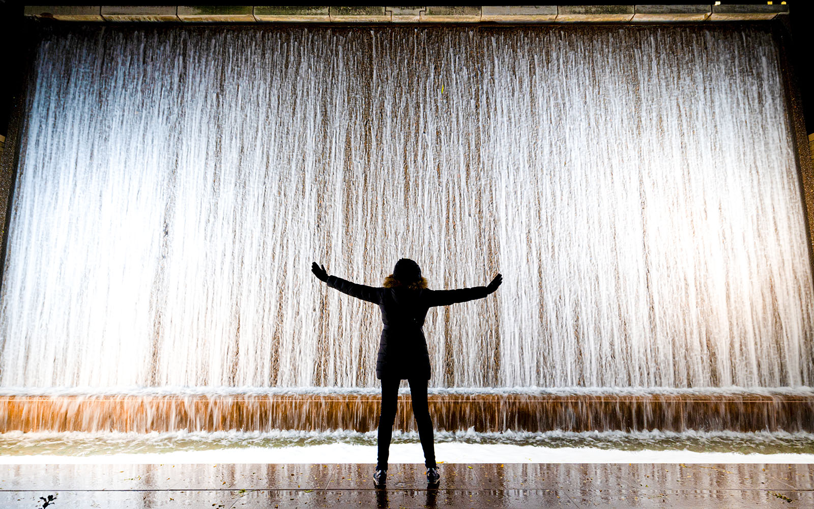 Silhouette of a woman with arms outstretched in front of Paley Park waterfall, New York City.