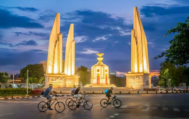 Cyclists ride past the illuminated Democracy Monument on a Bangkok night tour.