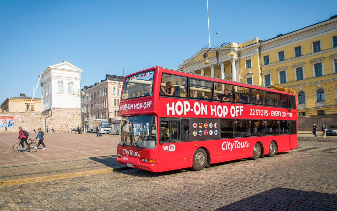 Hop on hop off tour bus in Helsinki's Senate Square with historic buildings.