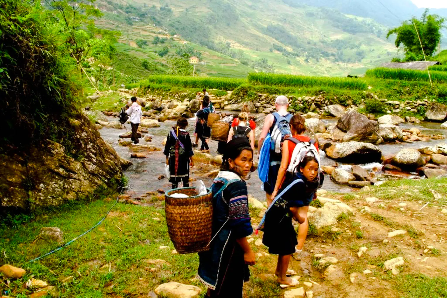 Tourists and locals crossing a stream in Sa Pa, Vietnam, during the Sapa Day Tour.