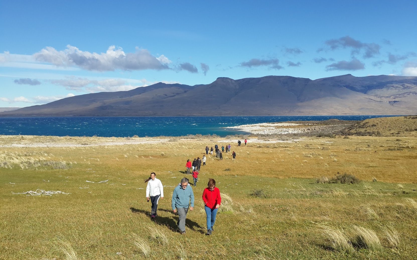 Tourists walking in Torres del Paine National Park, Chile, with mountains and lake in the background.
