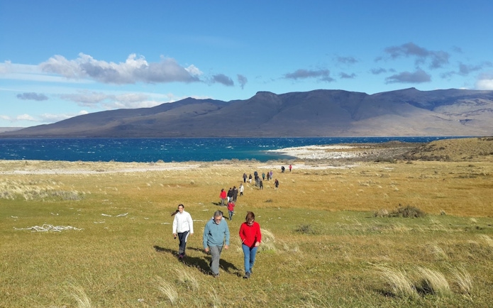 Tourists walking in Torres del Paine National Park, Chile, with mountains and lake in the background.