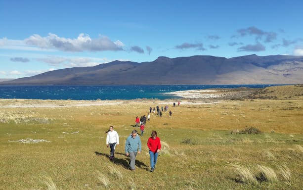 Tourists walking in Torres del Paine National Park, Chile, with mountains and lake in the background.