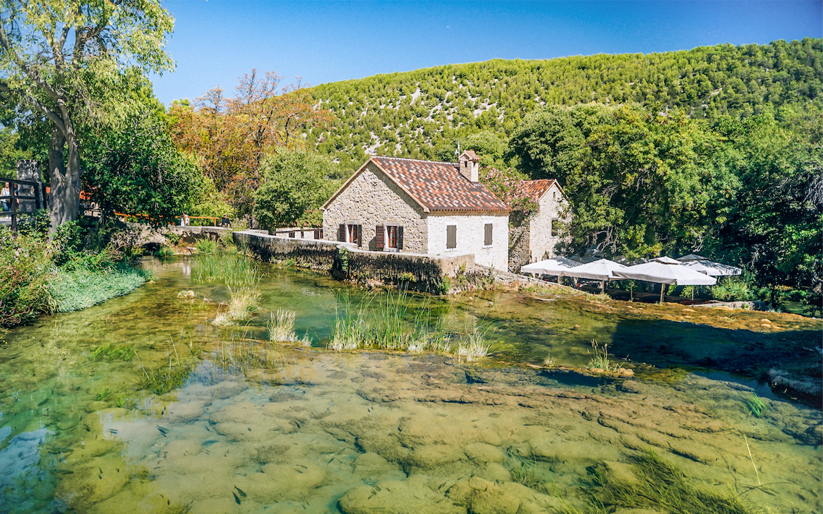 Stone house by a clear stream in Krka National Park, Croatia, surrounded by lush greenery.