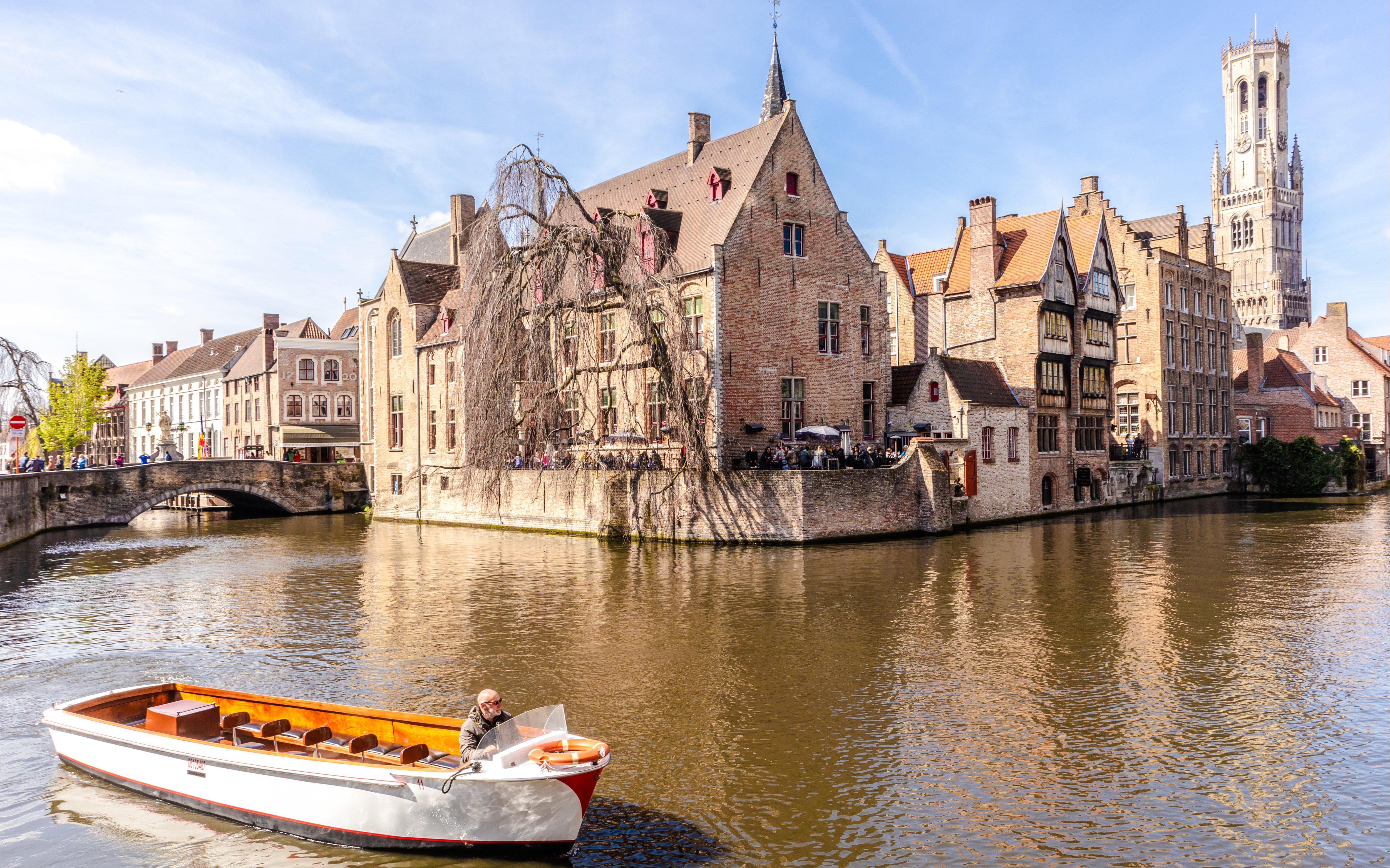 Boat on canal with historic buildings and Belfry tower in Bruges, Belgium.