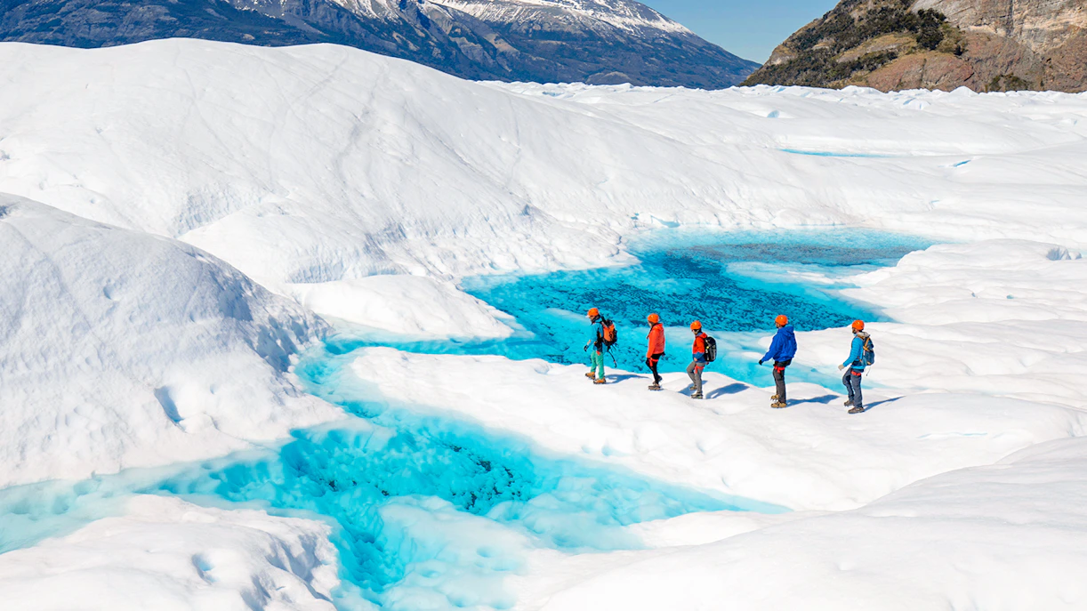 Tourists hiking on Perito Moreno Glacier with vibrant blue ice pools in Patagonia, Argentina.