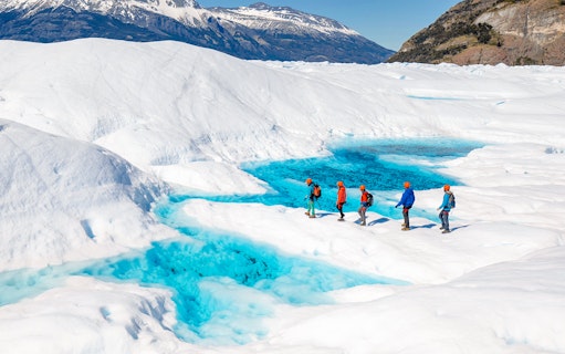 Tourists hiking on Perito Moreno Glacier with vibrant blue ice pools in Patagonia, Argentina.