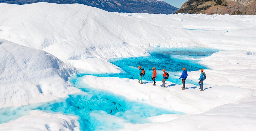 Tourists hiking on Perito Moreno Glacier with vibrant blue ice pools in Patagonia, Argentina.