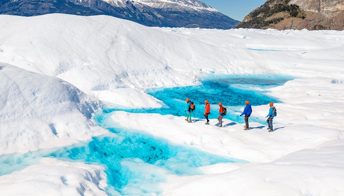 Tourists hiking on Perito Moreno Glacier with vibrant blue ice pools in Patagonia, Argentina.