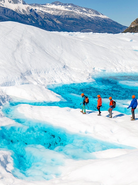 Tourists hiking on Perito Moreno Glacier with vibrant blue ice pools in Patagonia, Argentina.
