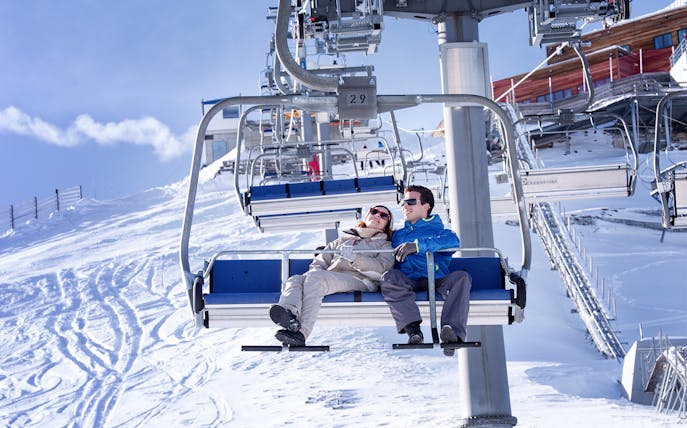Couple on cable car at Glacier 3000 with snowy mountain backdrop.