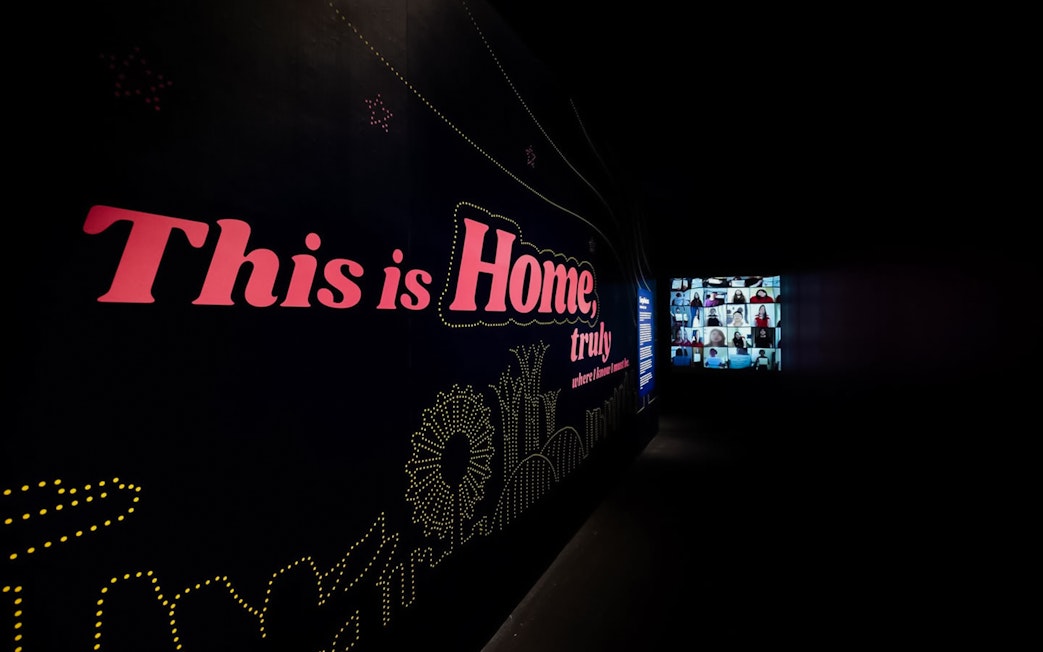 Large dark wall with "This is Home, truly" text and distant video screen.