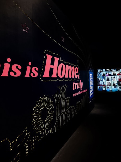 Large dark wall with "This is Home, truly" text and distant video screen.