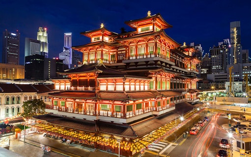 Chinese temple illuminated at night in Singapore's Chinatown with city skyline.